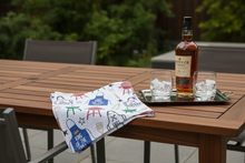 Load image into Gallery viewer, Father's Day BBQ kitchen towel angled on an upscale hardwood outdoor table with a bottle of Scotch whisky and two crystal glasses with ice on a tray, muted greenery in background